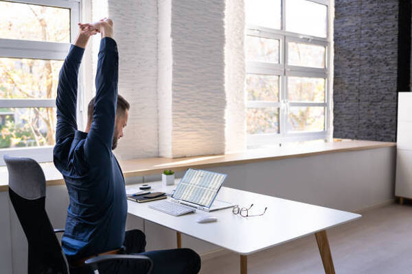 Person at a desk in a bright office reaching arms overhead in a gentle stretch